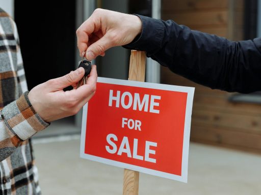 Close-up of a home for sale sign with people exchanging keys.