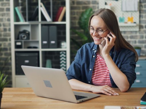 a woman talking on a cell phone while using a laptop