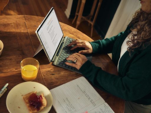 Woman typing on laptop at wooden table with breakfast.